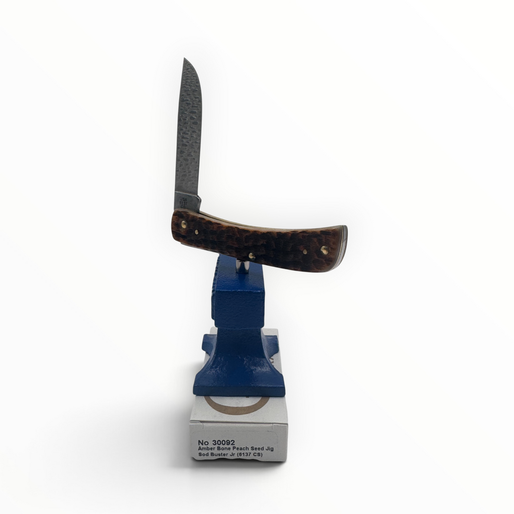 Pigeon Roost Knives Case XX Sod Buster Jr pocket knife with amber bone handle and carbon steel blade on a blue anvil