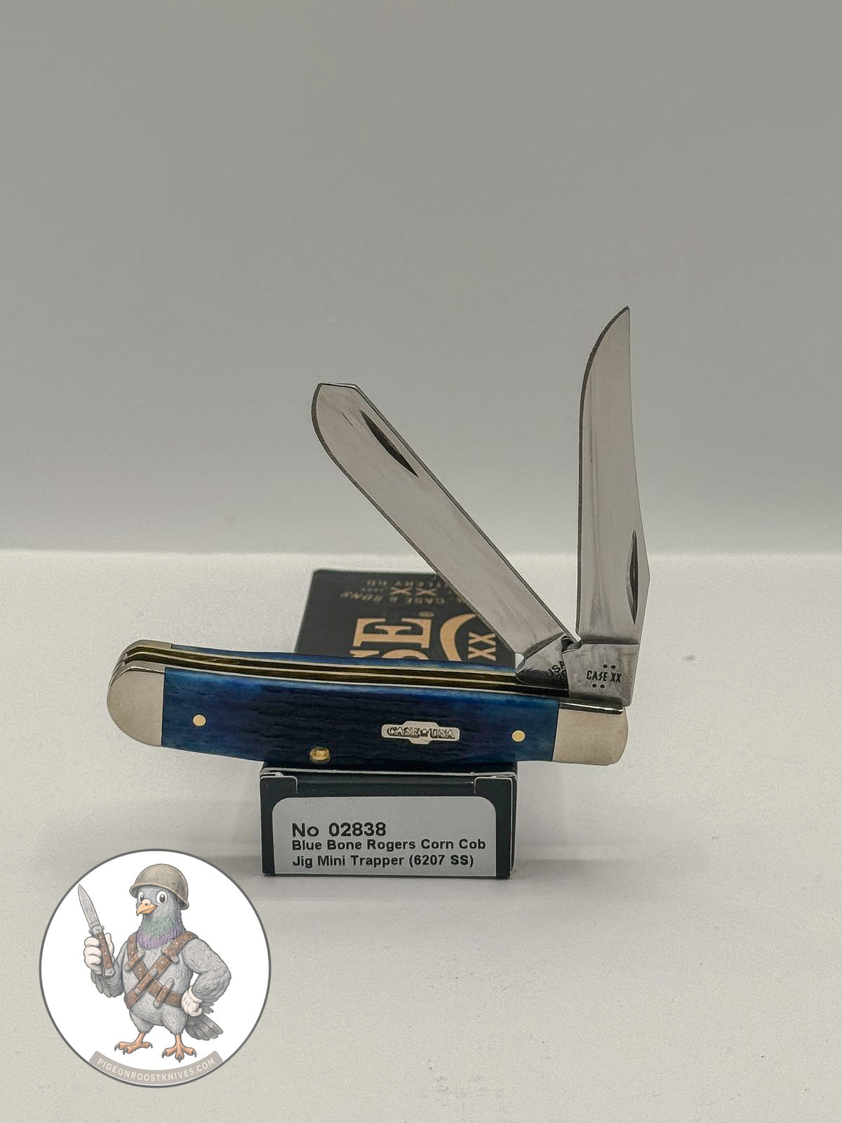 Case XX Mini Trapper with jigged navy blue bone and clip and spey blades, SKU 02838 — blades open resting on the factory box